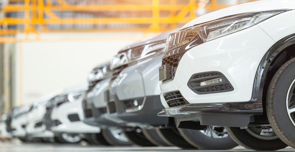 Reihe neuer Autos in heller Werkshalle, dicht nebeneinander geparkt.